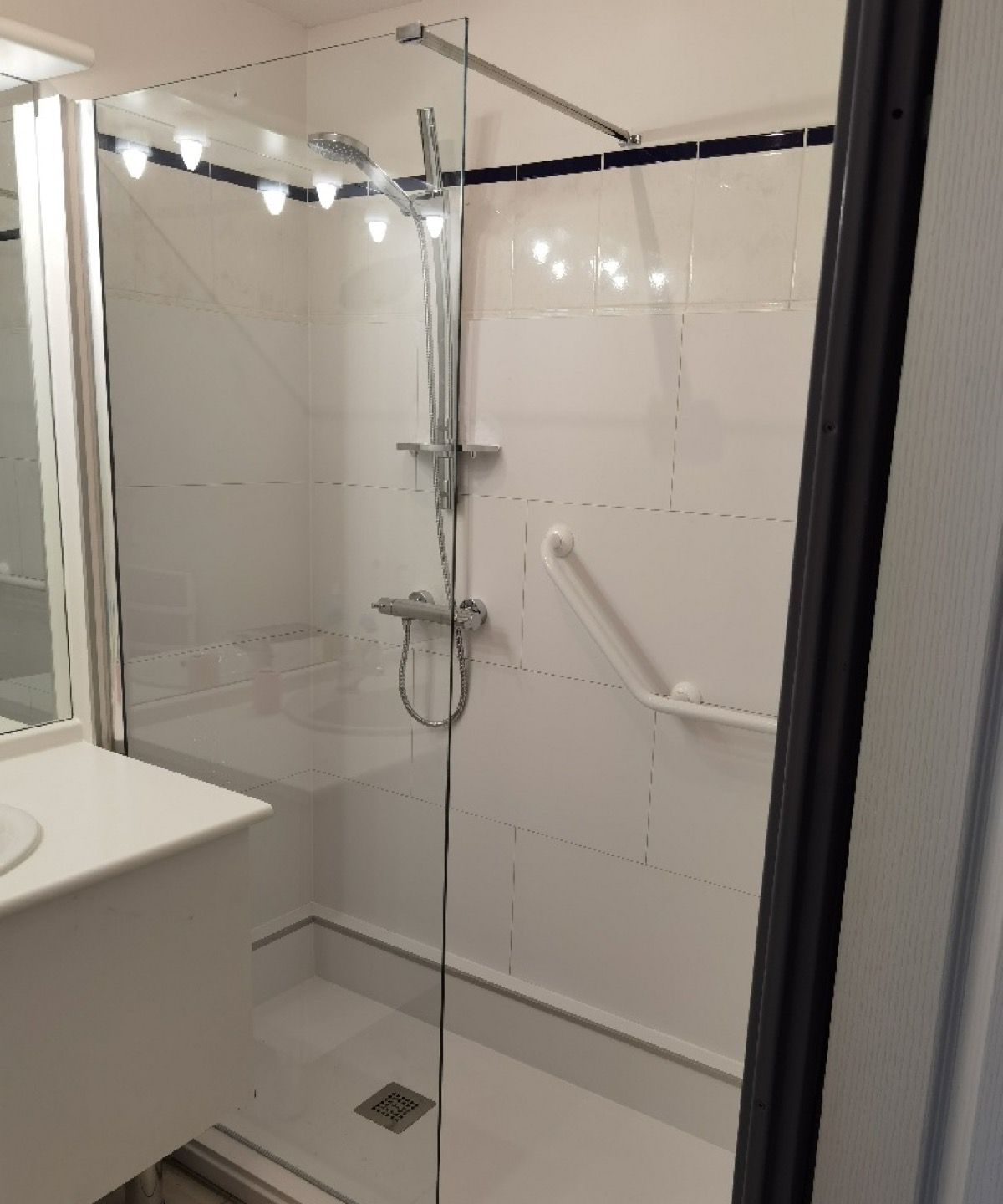 Salle d'eau rénovée : douche avec paroi vitrée, robinetterie thermostatique et barre de maintien